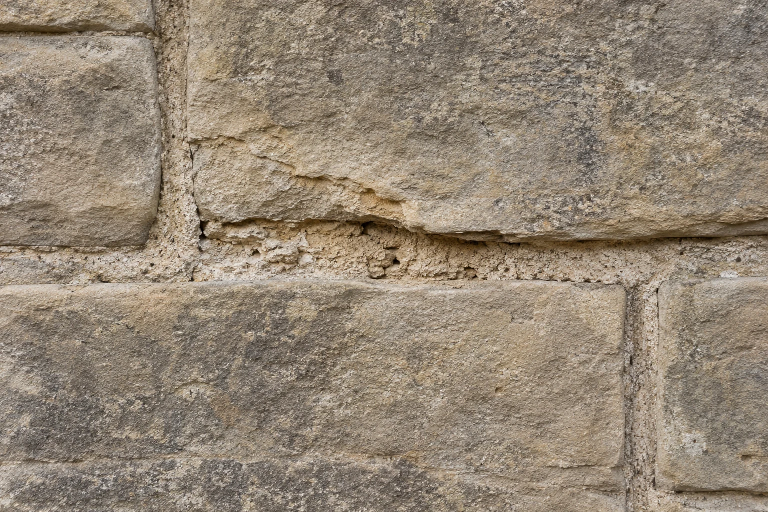 Recessed mortar and a flaking edge between sandstone blocks.